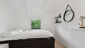 Ein Schlafzimmer mit Bett, Schminktisch, einem Fenster mit Blick auf Grünflächen und einem runden Spiegel an der Wand.