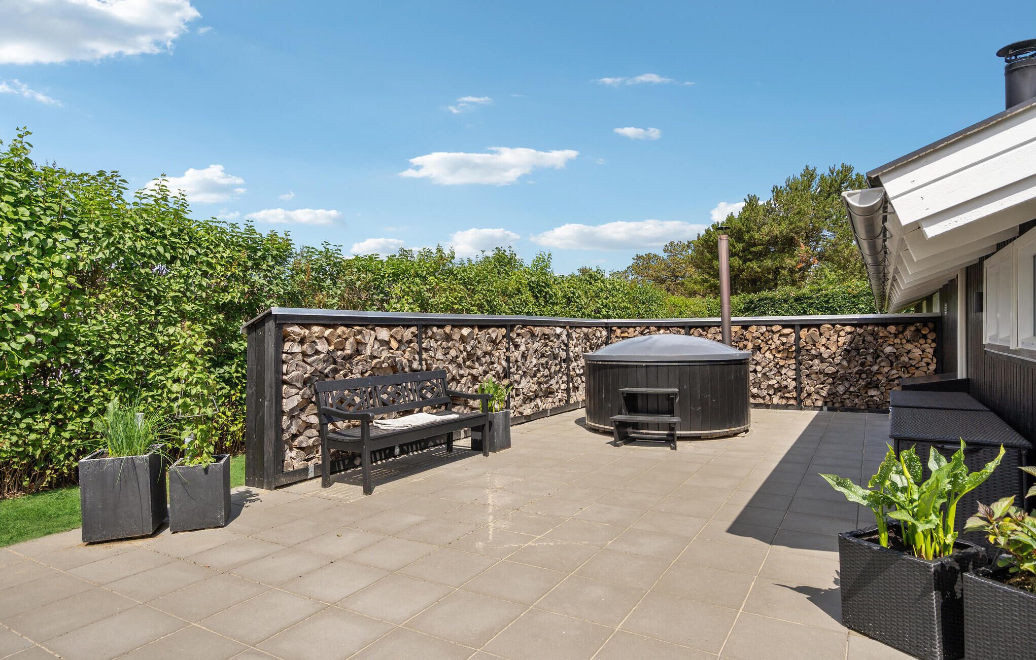 Un patio con pared de piedra, banca de madera, barbacoa y plantas en macetas.