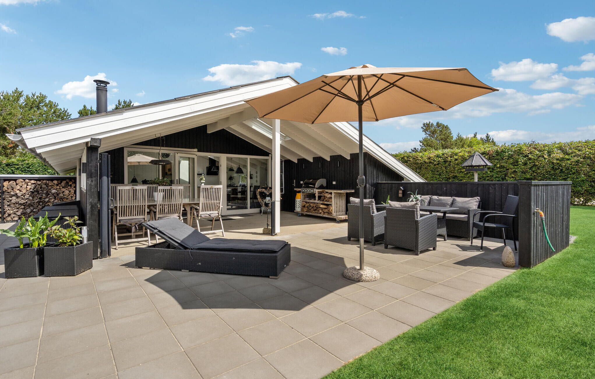 A covered outdoor patio with seating, a barbecue area, and a pergola with an umbrella.