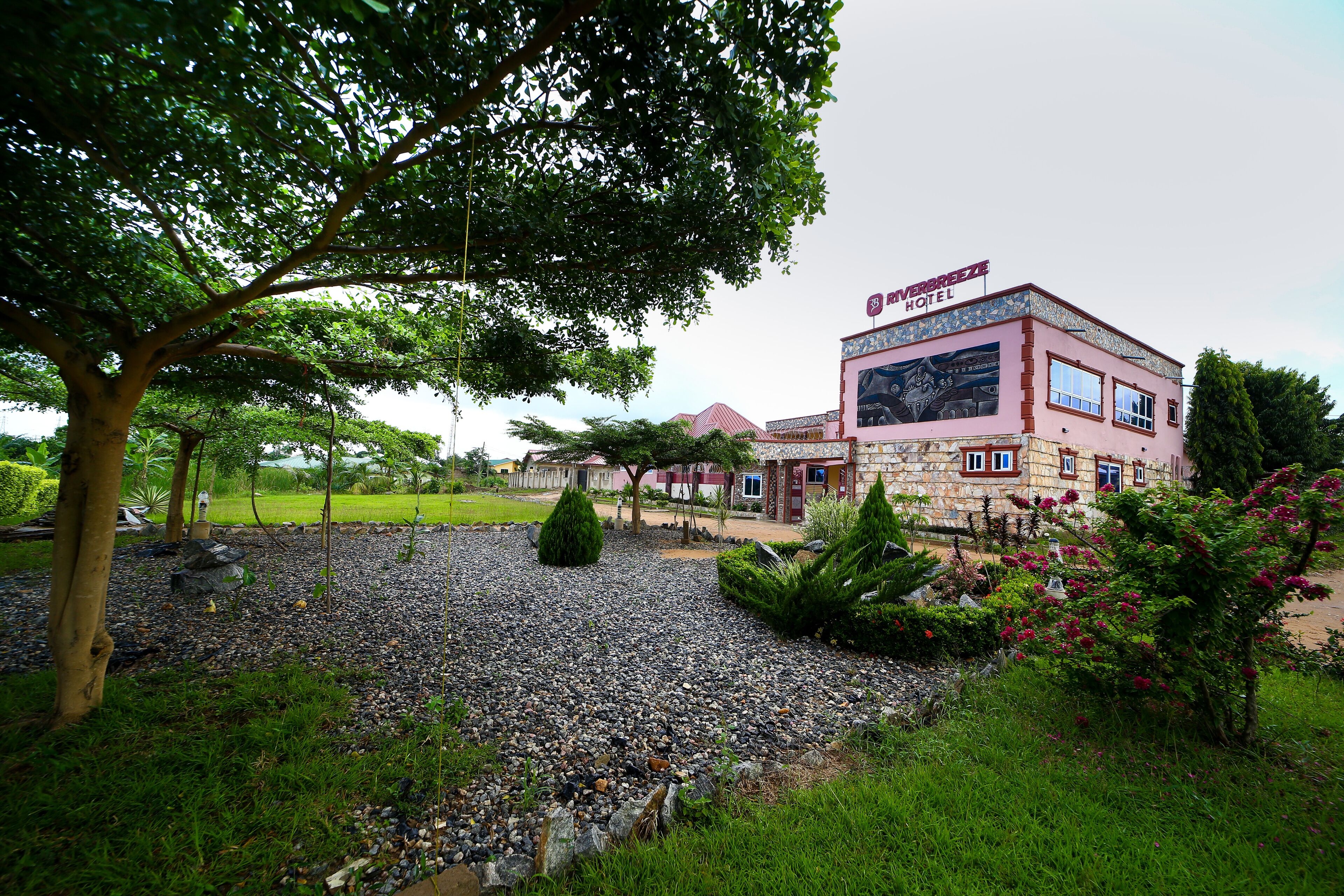 A hotel with a sign reading "VERBRAEZE HOTEL" and a garden with a gravel path and greenery.