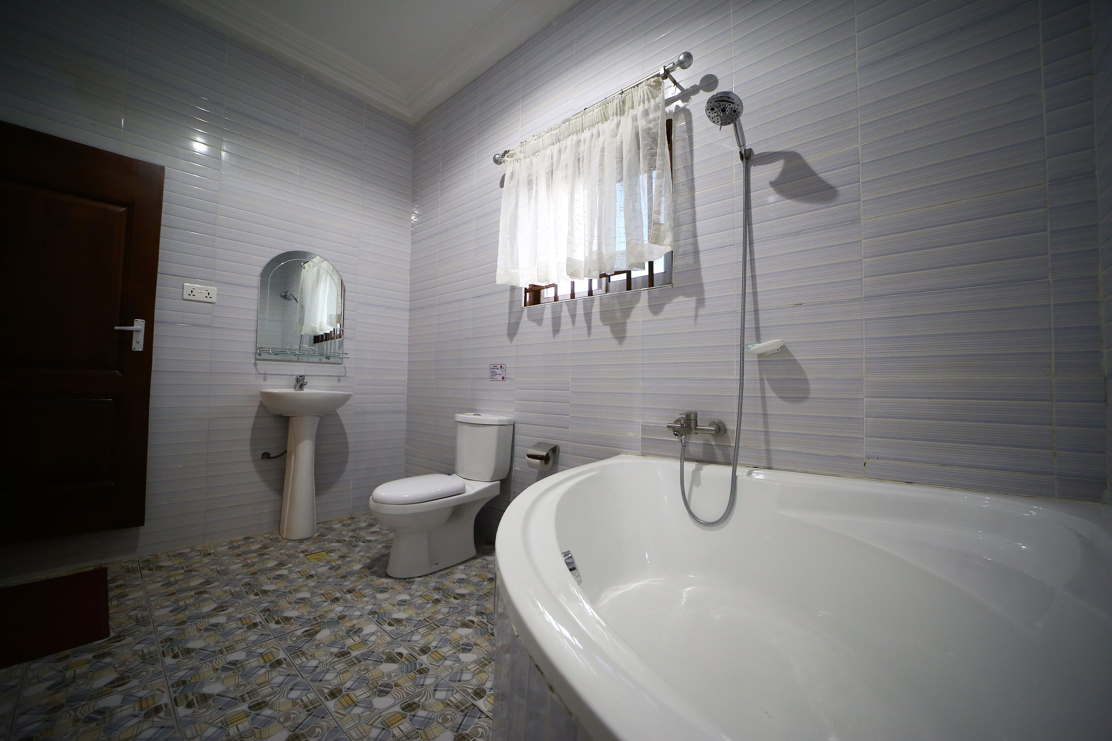 Et badeværelse med et hvidt badekar, toilet, vask og spejl.