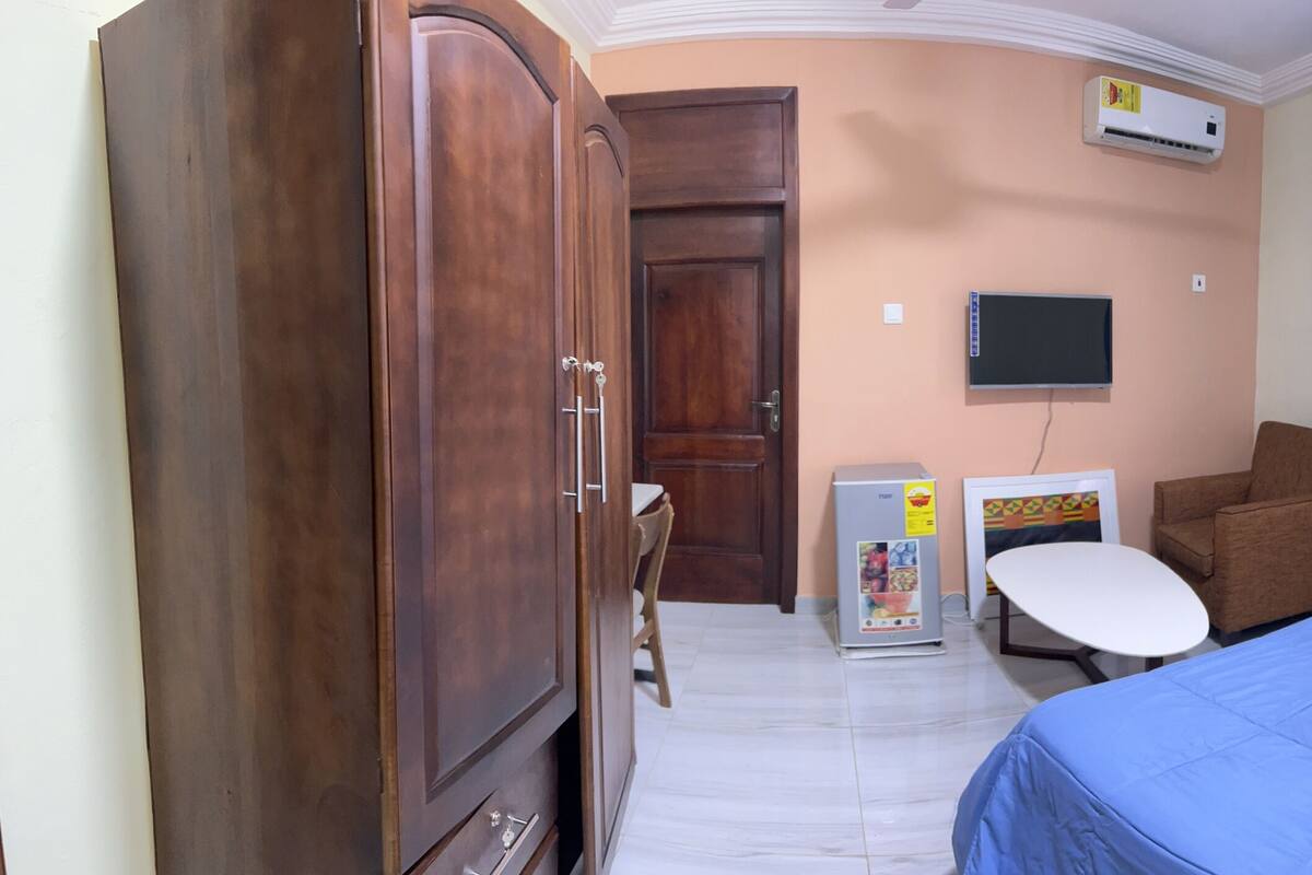 A hotel room with a bed, a desk, a chair, a wardrobe, and a television.