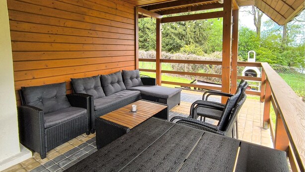 An outdoor patio with wicker furniture, a wooden table, and a pergola structure. - Gorgeous home in Morag with lake view (Morag)