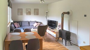 A living room with a sofa, TV, table, chairs, and a wood-burning stove. - Gorgeous home in Morag with lake view (Morag)