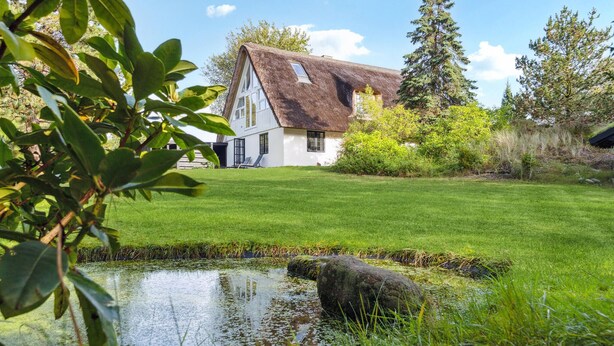 A house with a thatched roof, surrounded by a well-maintained lawn and a pond. - Lake front home in Rømø with WiFi (Rømø)
