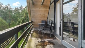 A balcony with a wooden railing, a small table with two chairs, and a glass door leading to a patio area. - Lake front home in Rømø with WiFi (Rømø)