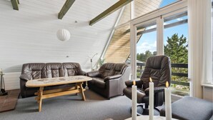A cozy room with a sofa, a small table, and a chair. There is a window with a view of trees and a fence. - Lake front home in Rømø with WiFi (Rømø)
