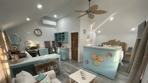 A modern kitchen with a dining area, a living room with a sofa and coffee table, and a bedroom with a bed and nightstand.