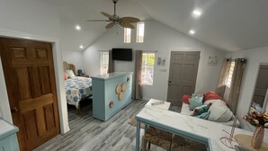 A cozy, well-lit room with a bed, a small kitchenette, a dining area, and a ceiling fan.