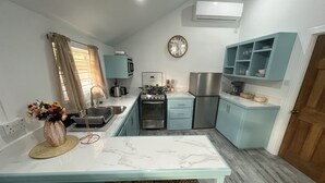 A compact kitchen with a central island, a sink, a stove, and a refrigerator. There are two wicker stools at the island.