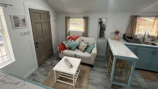 A compact living space with a sofa, a small table, a kitchen area, and a window with curtains.