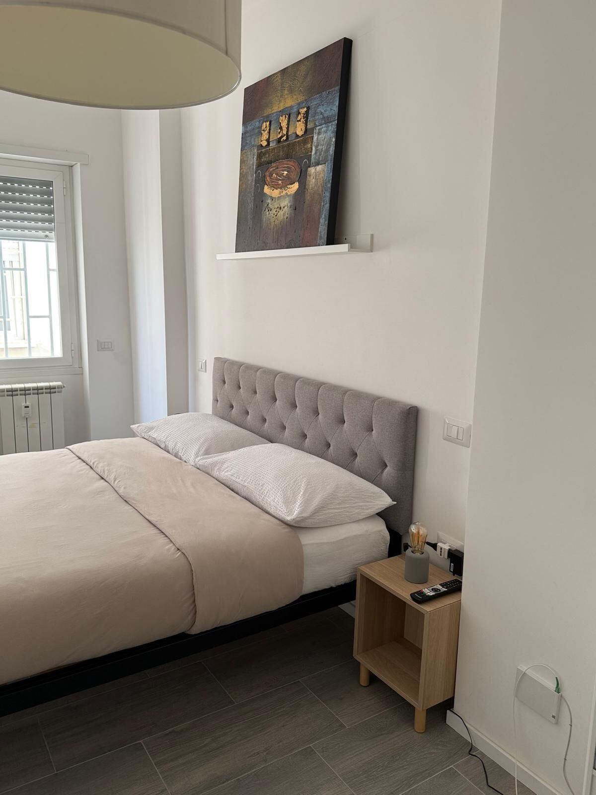 A bedroom with a bed, a headboard, a bedside table, and a wall-mounted artwork.