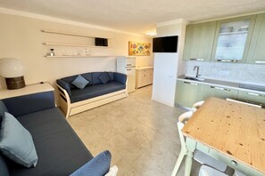 A compact living space with a sofa, a wooden dining table, a kitchenette, and a small cabinet.