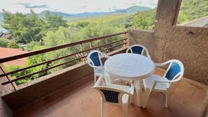 A balcony with a round table and four chairs, overlooking a lush green landscape with trees and hills. - Superior two-room apartment with 4 beds (40 m2) with living-dining room and double sofa bed or two separate sofa beds or 2 built-in beds, double bedroom.The apartments have an outdoor space (balcony if on the first floor and terrace if on the ground floo (Olbia)