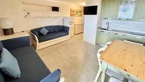 A compact living space with a sofa, a wooden dining table, a kitchenette, and a small cabinet. - Superior two-room apartment with 4 beds (40 m2) with living-dining room and double sofa bed or two separate sofa beds or 2 built-in beds, double bedroom.The apartments have an outdoor space (balcony if on the first floor and terrace if on the ground floo (Olbia)