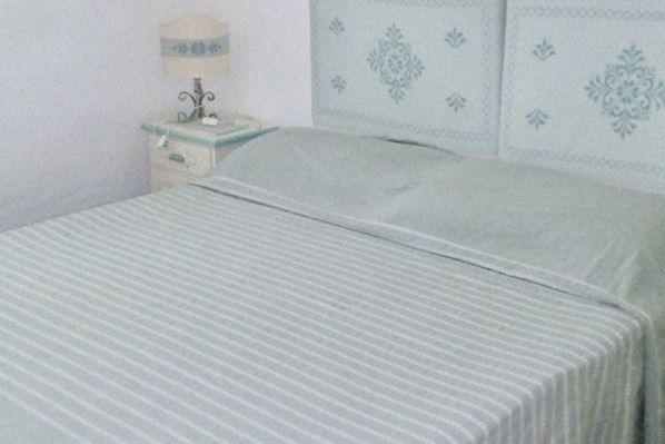 A bed with a striped bedspread, a bedside table with a lamp, and a wall with decorative paneling.