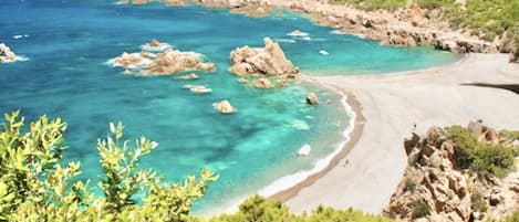 Paisaje costero con aguas turquesas cristalinas, formaciones rocosas y una playa arenosa.