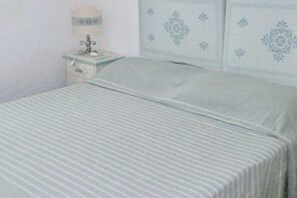 A bed with a striped bedspread, a bedside table with a lamp, and a wall with decorative paneling.