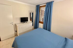Ein Schlafzimmer mit einem Bett, einem Schminktisch, einem Fernseher und einem Fenster mit Vorhängen.