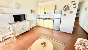 A compact kitchen with yellow cabinets, a white refrigerator, and a stove. There's a dining area with a table and chairs, and a television on a stand. - Superior two-room apartment with 4 beds (40 m2) with living-dining room and double sofa bed or two separate sofa beds or 2 built-in beds, double bedroom.The apartments have spaceoutside (balcony if on the first floor and terrace if on the ground floor) w (Olbia)
