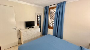 A bedroom with a bed, a dresser, a television, and a window with curtains. - Superior two-room apartment with 4 beds (40 m2) with living-dining room and double sofa bed or two separate sofa beds or 2 built-in beds, double bedroom.The apartments have spaceoutside (balcony if on the first floor and terrace if on the ground floor) w (Olbia)