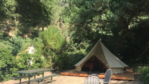 A tented camping area with a picnic table and chairs, surrounded by dense forest. - Sequoia Jewel -16 Foot Bell Tent with double beds. 4.5 to Sequoia National Park. (Three Rivers)