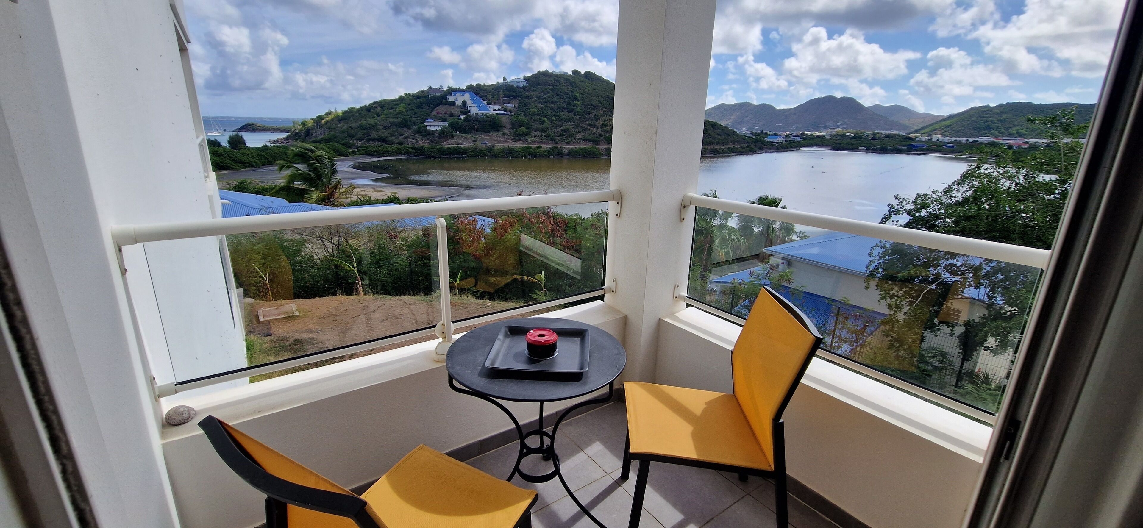 Uma varanda com mesa e cadeiras, com vista para um lago e colinas.