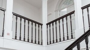 Una imponente escalera con columnas blancas y balaustradas oscuras, que conduce a un nivel superior con un amplio ventanal de arco.