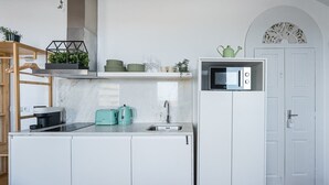Una cocina compacta con armarios blancos, microondas integrado, hervidor y tostadora.
