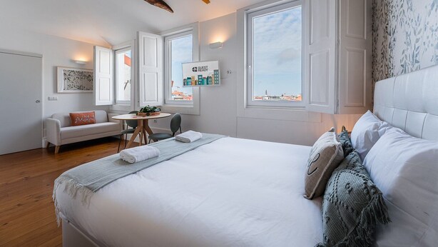 Habitación de hotel con una cama grande, una mesita, un sofá y una ventana con vista a la ciudad.