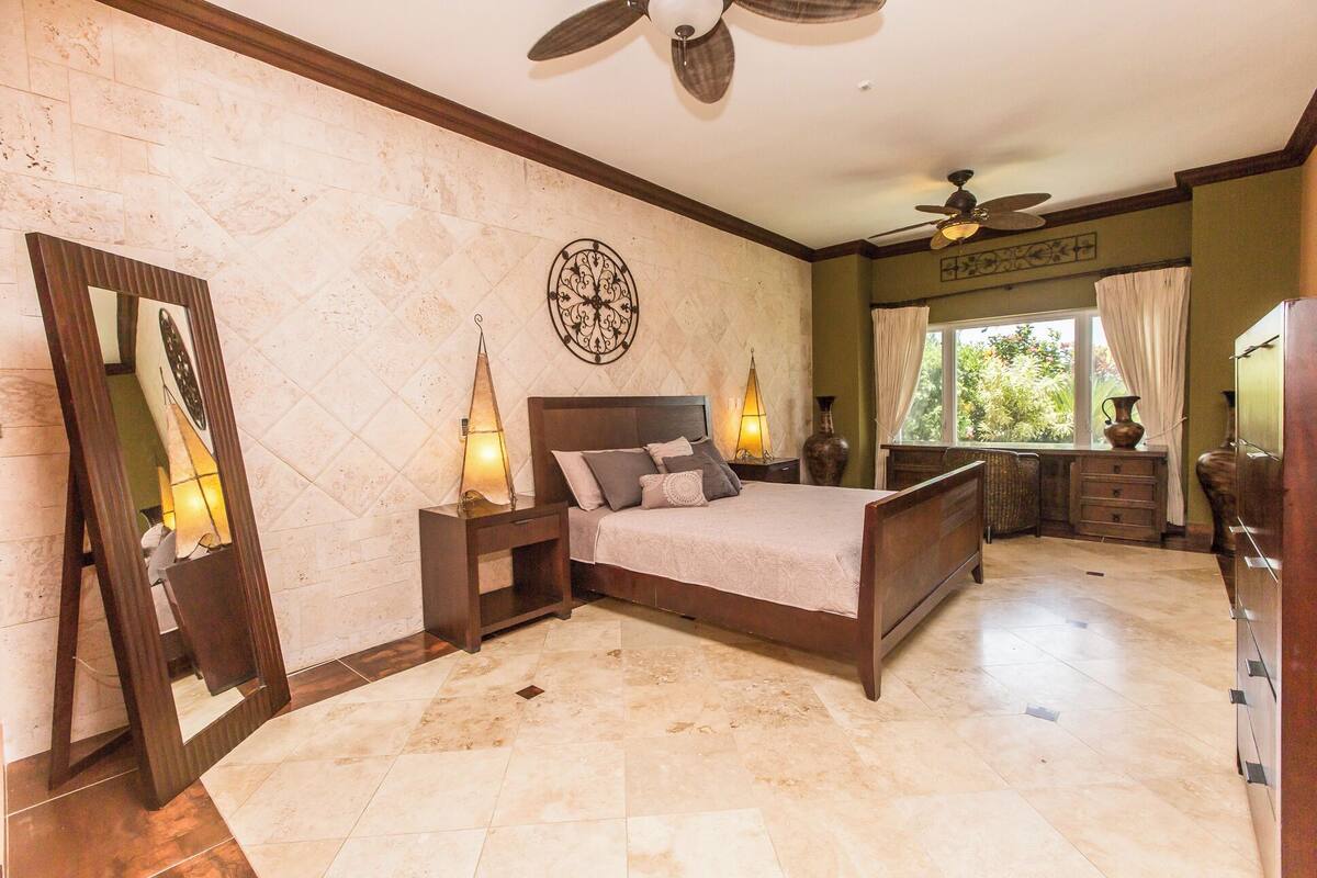 A bedroom with a bed, nightstands, a mirror, a ceiling fan, and a window with curtains.