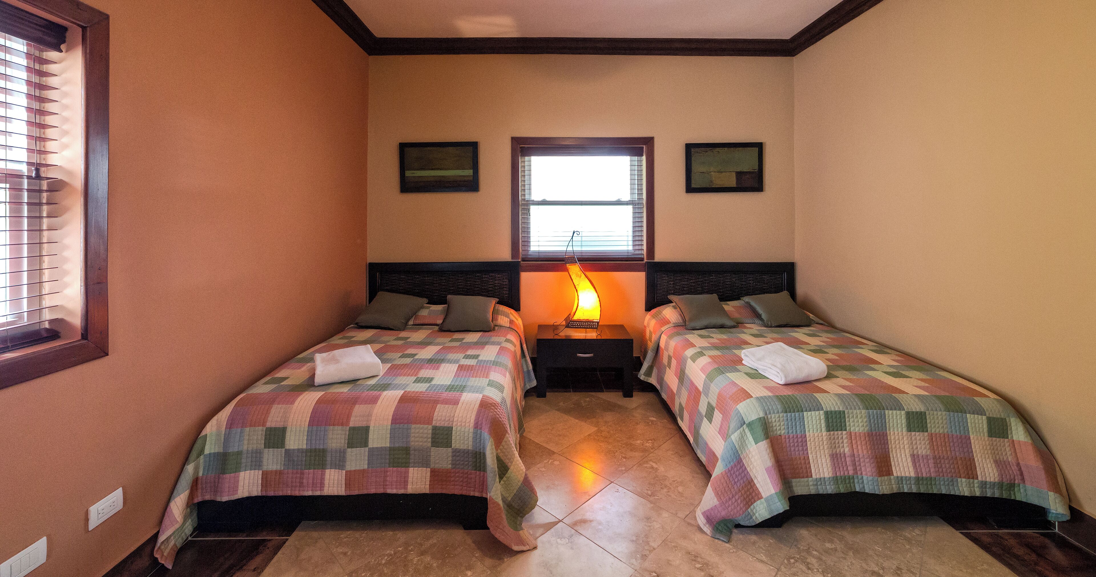 A room with two beds, a nightstand, a lamp, and a window with blinds.