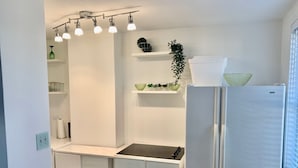 A modern kitchen with white cabinets, a stainless steel refrigerator, and a built-in sink. There are shelves with plants and decorative items. - ATL Downtown Condo w Balcony with City views (Atlanta)
