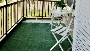 A balcony with a green artificial turf floor, a white table with a potted plant, and a metal railing. - ATL Downtown Condo w Balcony with City views (Atlanta)