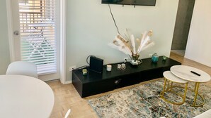 A modern living room with a flat-screen TV mounted on the wall, a black entertainment unit with decorative items, a white round table, and a patterned rug. - ATL Downtown Condo w Balcony with City views (Atlanta)