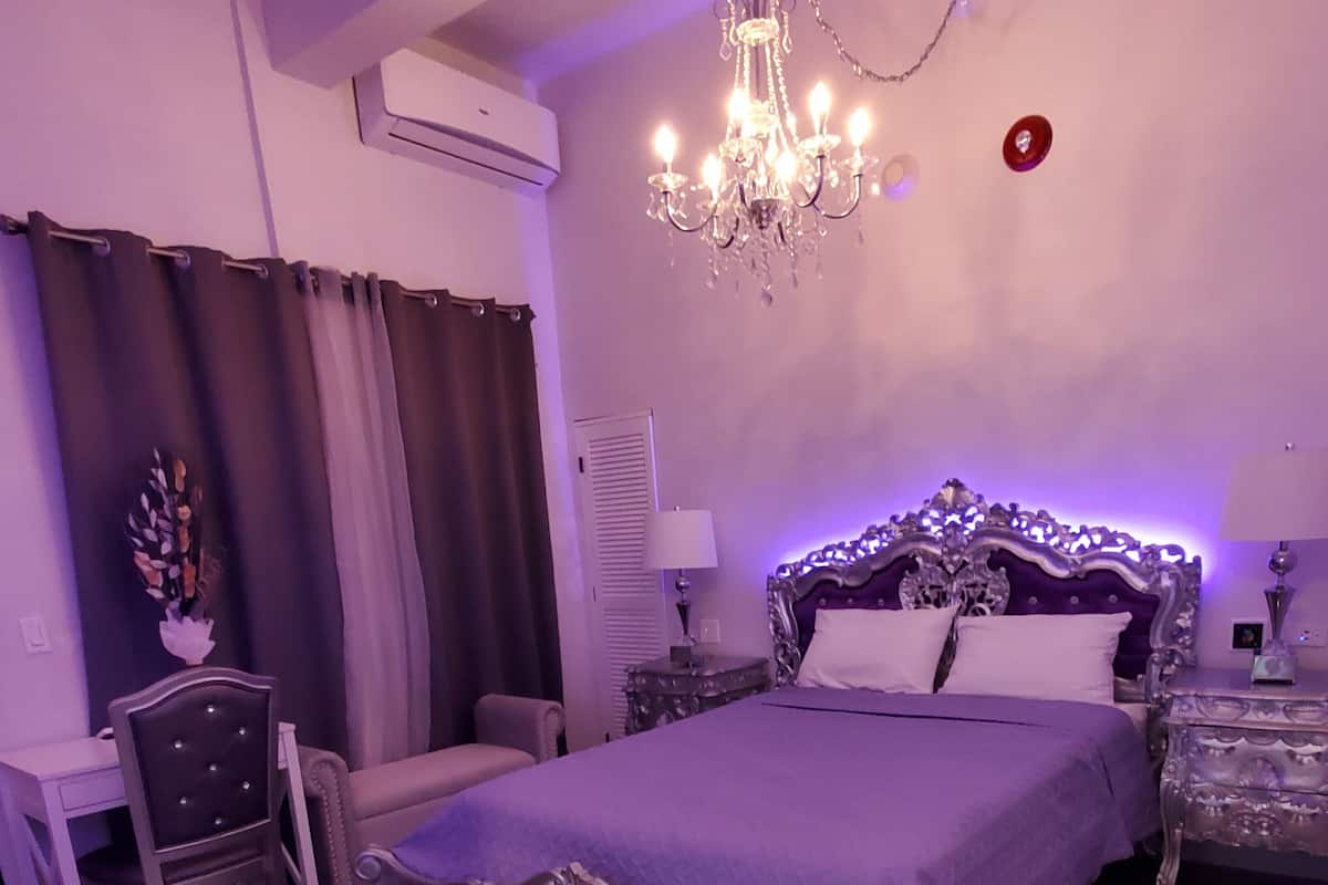 A bedroom with a large bed, a chandelier, a desk, and a chair.
