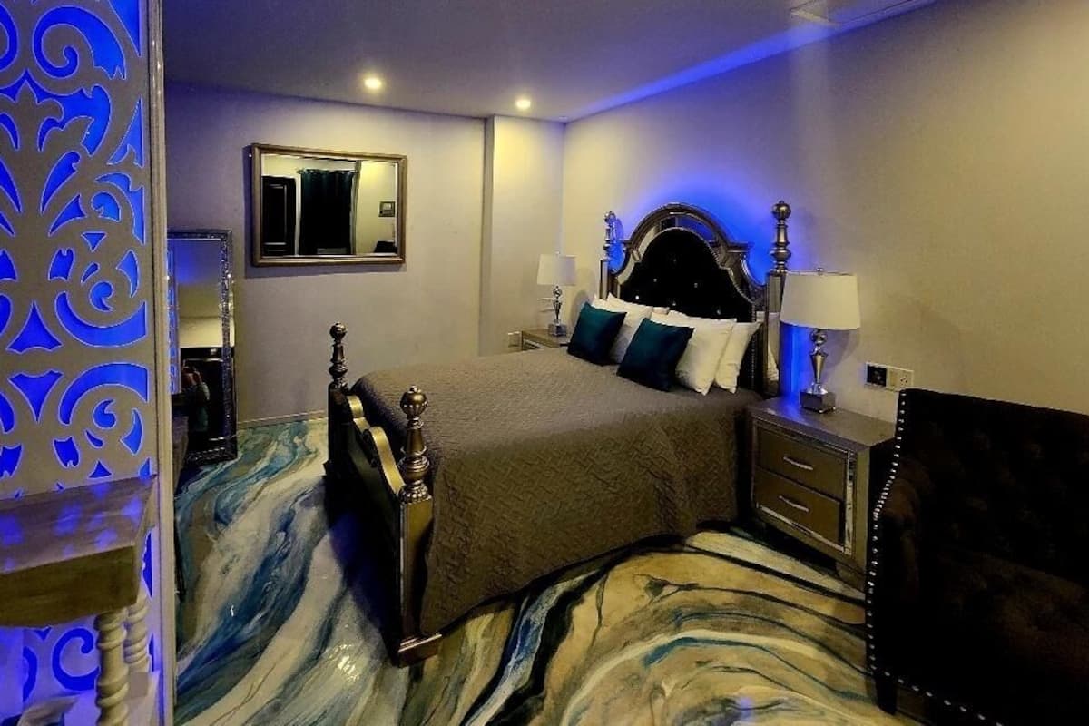 A bedroom with a large bed, a nightstand, a dresser, a mirror, and a decorative wall panel.