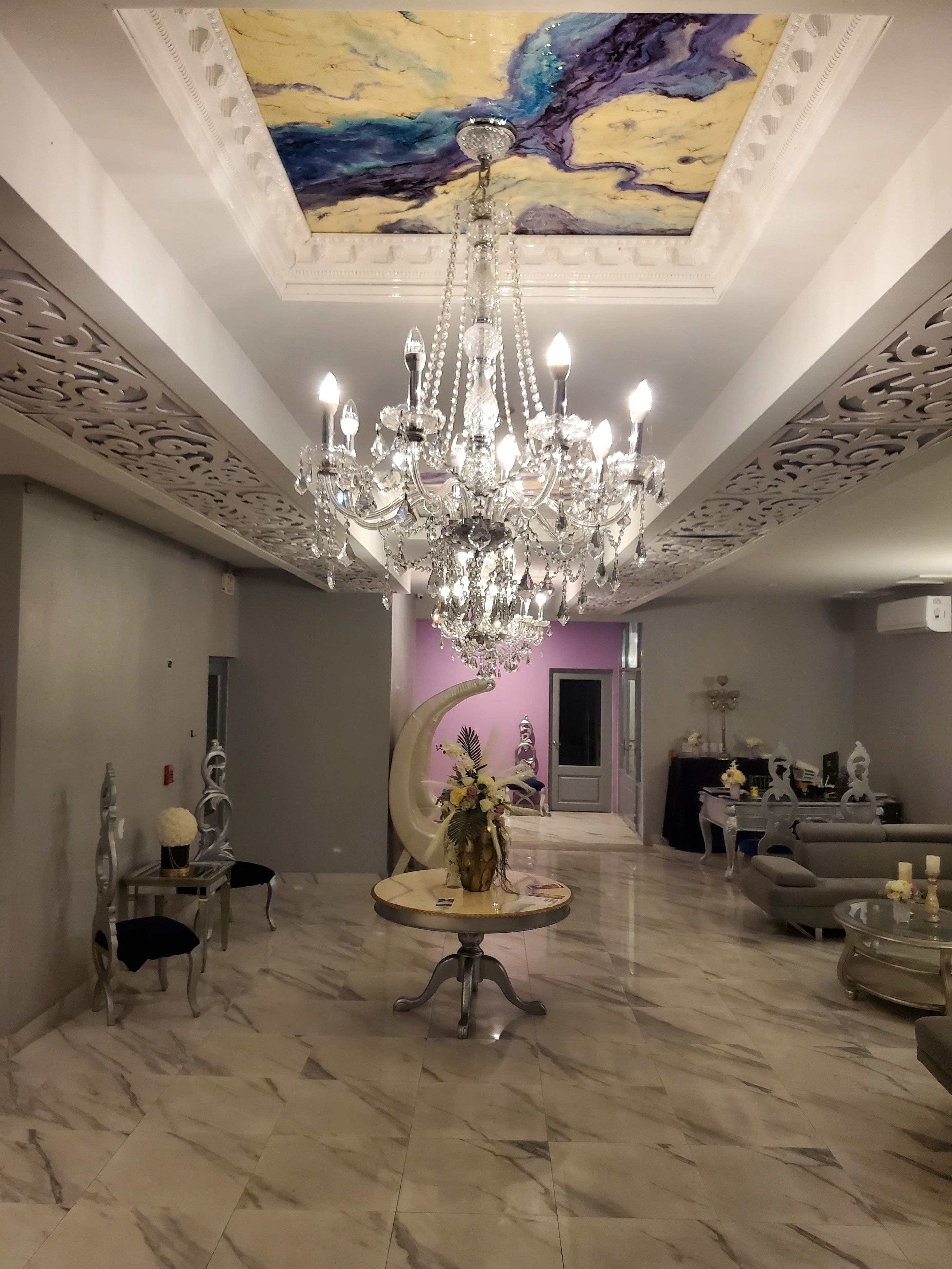 A spacious lobby with a large chandelier, marble flooring, and a unique ceiling design.