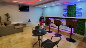 A bar area with a green wall, bar stools, and a counter with a neon light. - Luxury Puerto Caribe Boutique Hotel (Aguada)