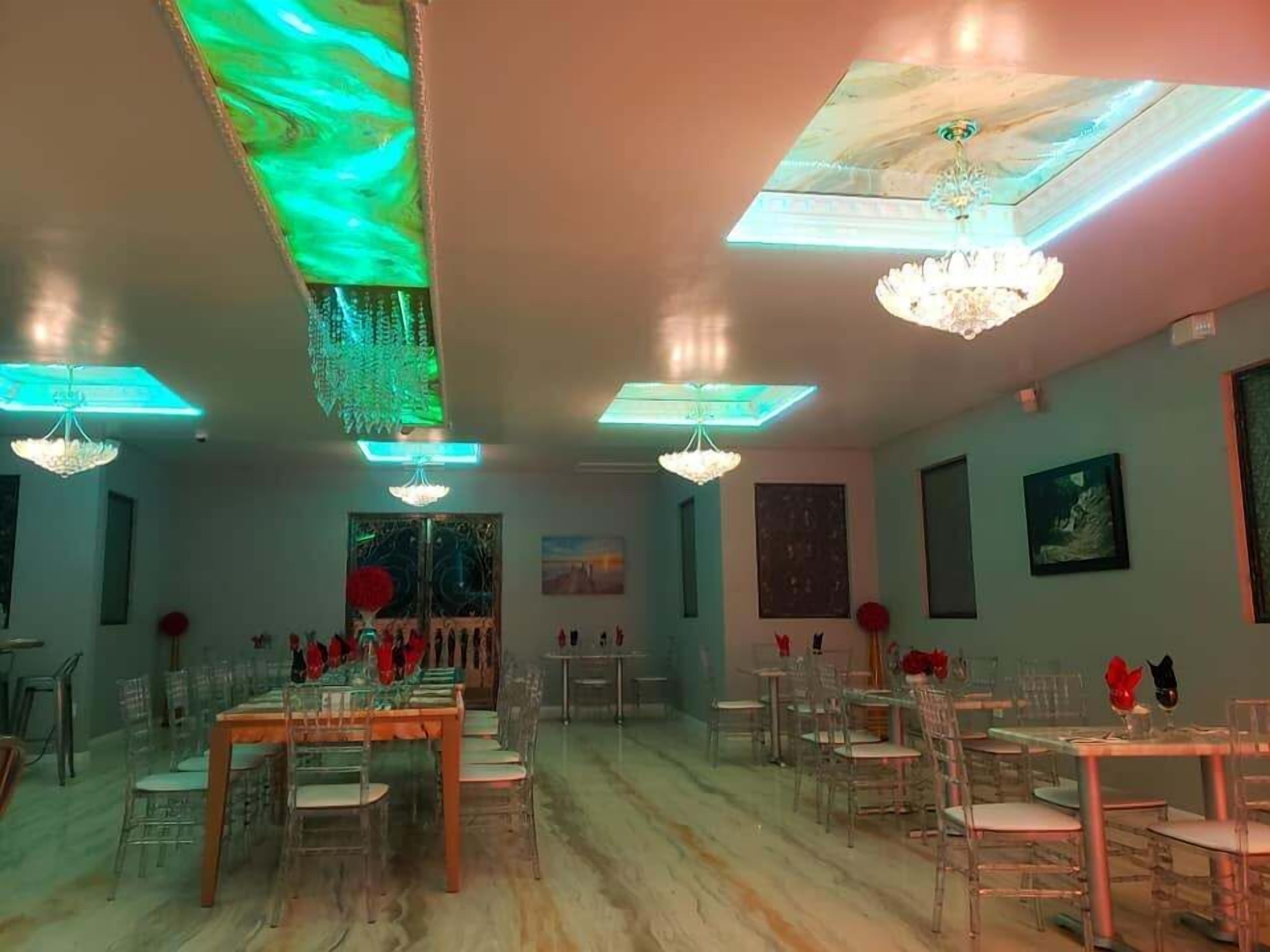 Un vaste espace dédié à la salle à manger, comprenant plusieurs tables et chaises, un lustre et un plafond doté de panneaux lumineux.