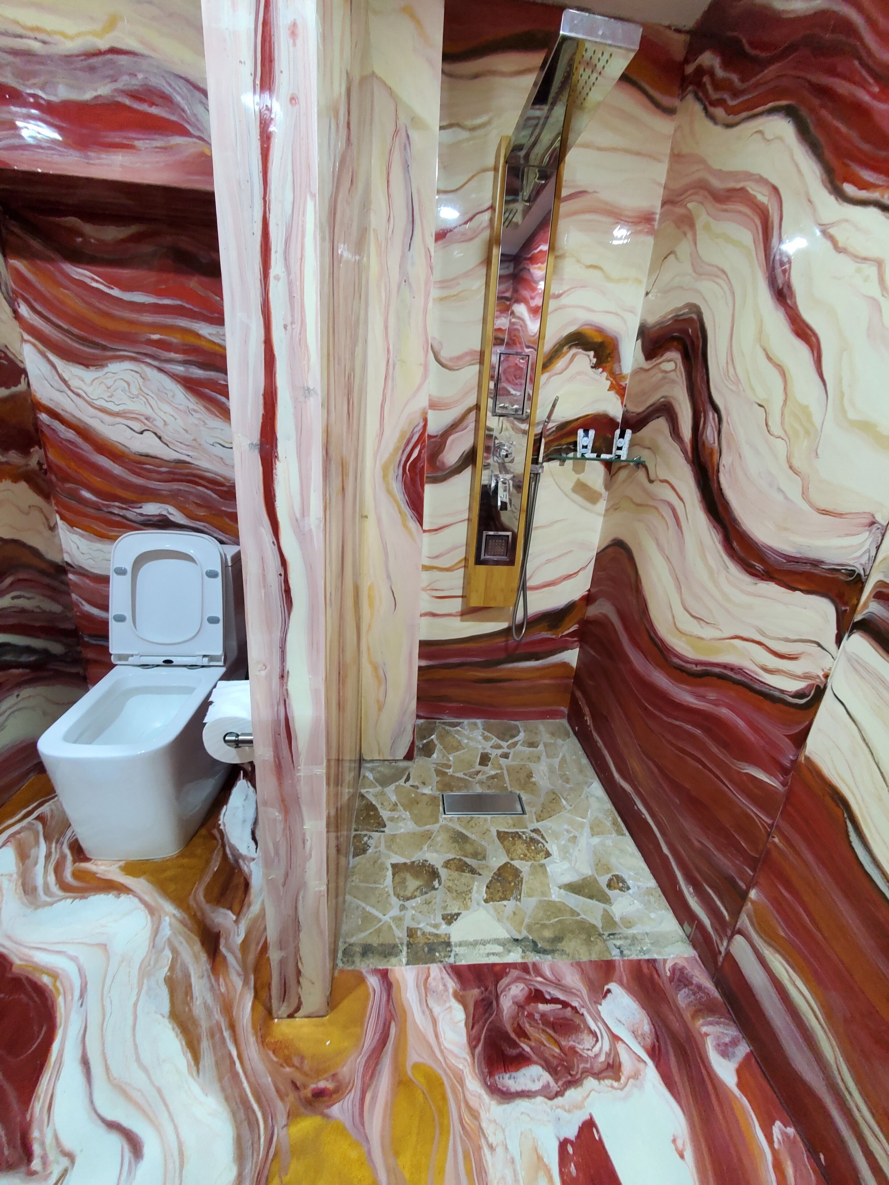 Et badeværelse med en marmorvægsdesign, et hvidt toilet og et spejl.