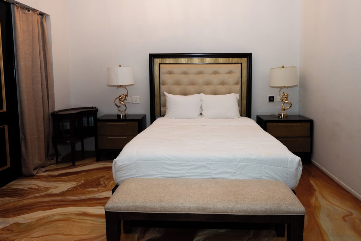 A neatly arranged hotel room with a large bed, two bedside tables with lamps, a bench, and a marble-patterned floor.
