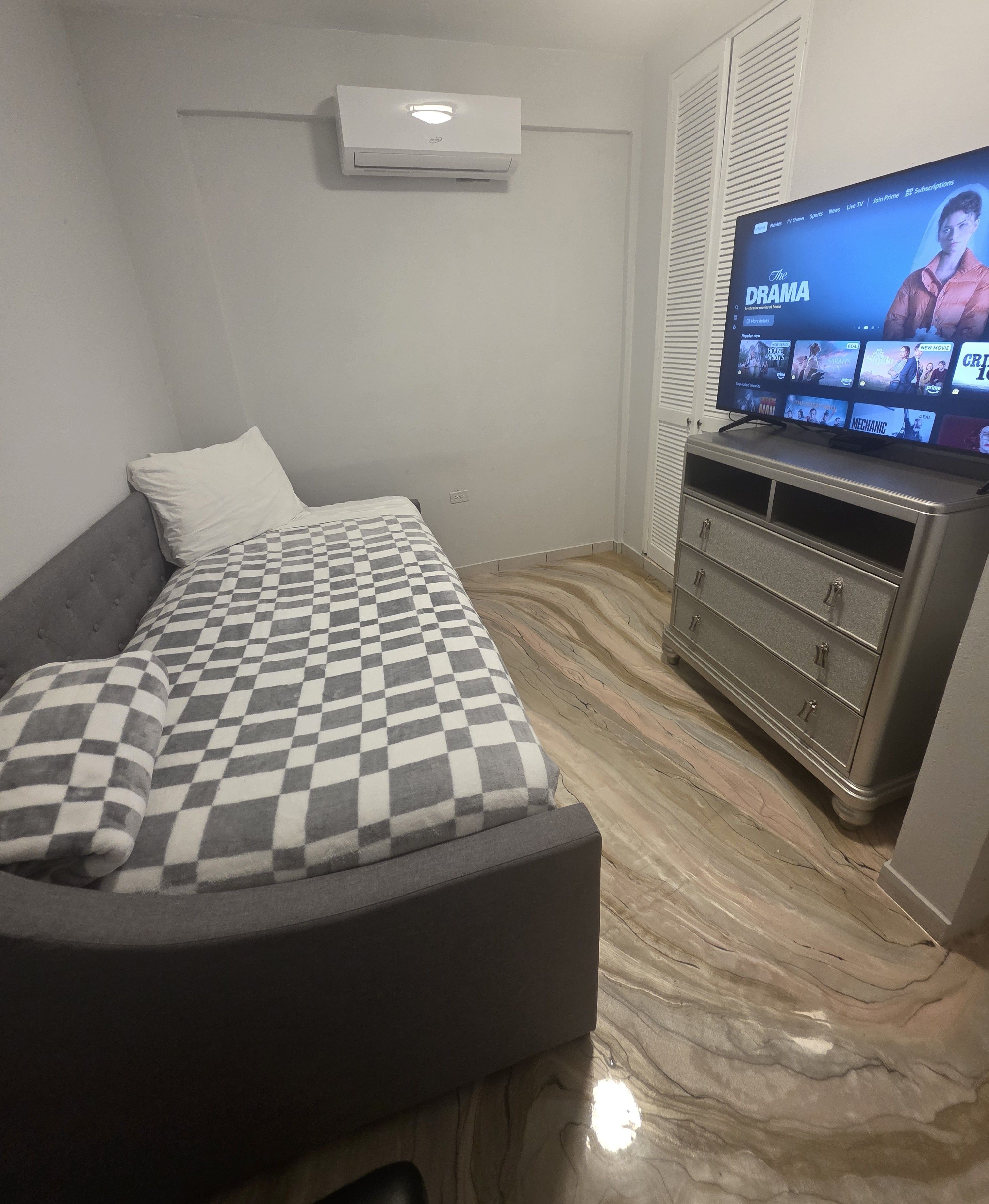 A bedroom with a bed, a dresser, and a television displaying a movie.