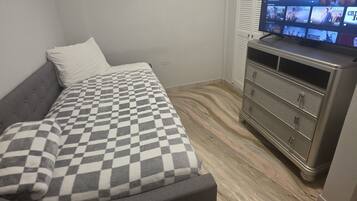 A bedroom with a bed, a dresser, and a television displaying a movie.