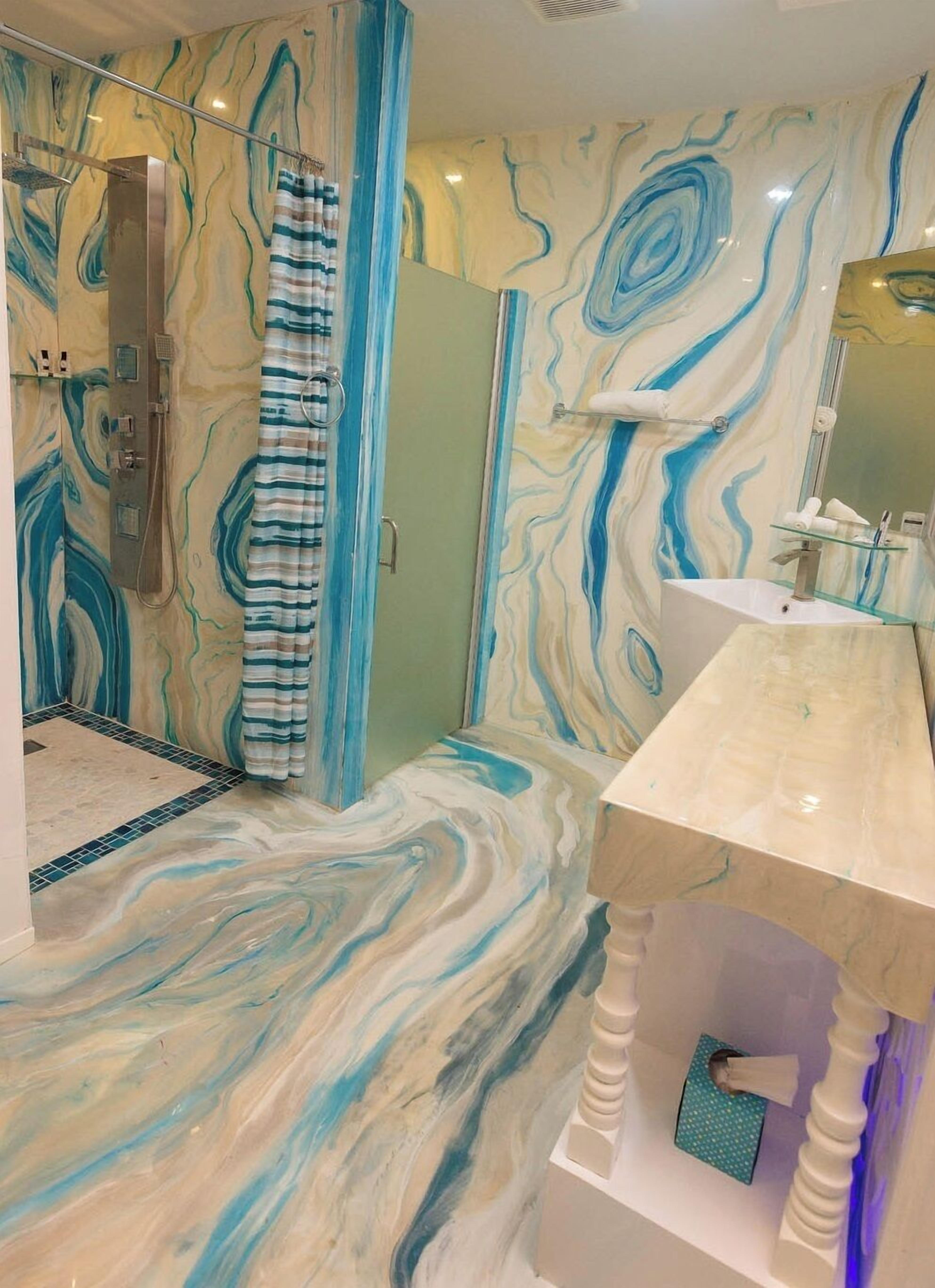 Un bagno con pavimento e pareti in marmo, una doccia con tenda a righe e un lavabo con ripiano in vetro.