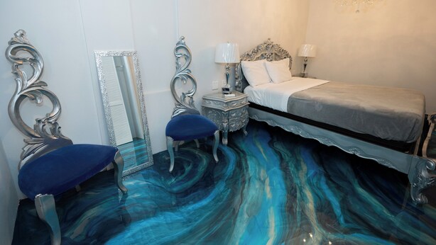 A bedroom with a bed, two nightstands, a chandelier, a mirror, and a blue upholstered bench. - Luxury Puerto Caribe Boutique Hotel (Aguada)