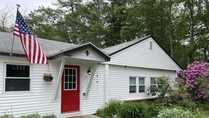 Une maison blanche avec une porte rouge, un drapeau américain et un porche agrémenté d’un paillasson.