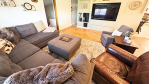 Un salon moderne avec un canapé d’angle, un fauteuil en cuir et un téléviseur à écran plat.