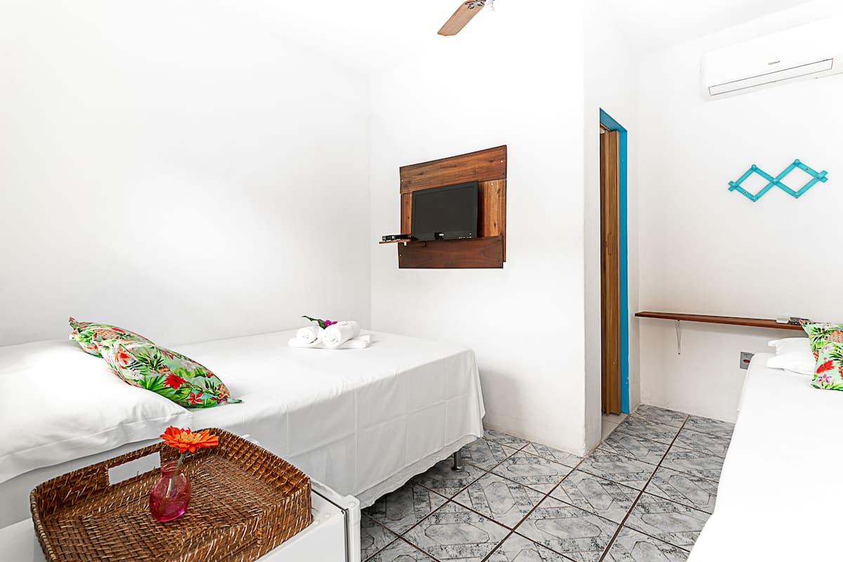 A small, clean room with two beds, a wooden-framed mirror, a wall-mounted air conditioner, and a tiled floor.