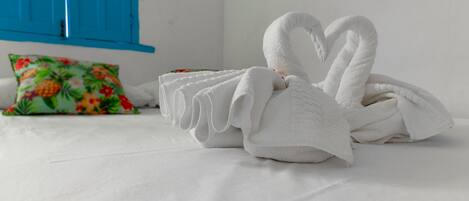 A bed with white linens and a swan-shaped towel arrangement.